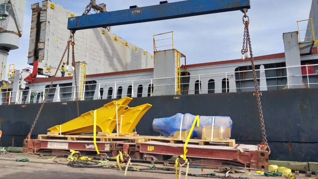 cargo_services_07 Cargo surveying and pre-shipment inspections of oversized yellow machinery being loaded onto a ship for transport. Zeus Marine and Cargo Solution cargo services ensuring safe and secure loading with proper securing methods. Cargo out-turn survey in progress to verify shipment conditions, and Stowage and Lashing Condition Survey